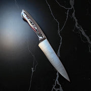  Tanzo Cutlery Kaizen 6 inch handcrafted utility knife with black white and red Fordite handle and brushed AEB-L stainless steel blade resting diagonally on a black marble surface