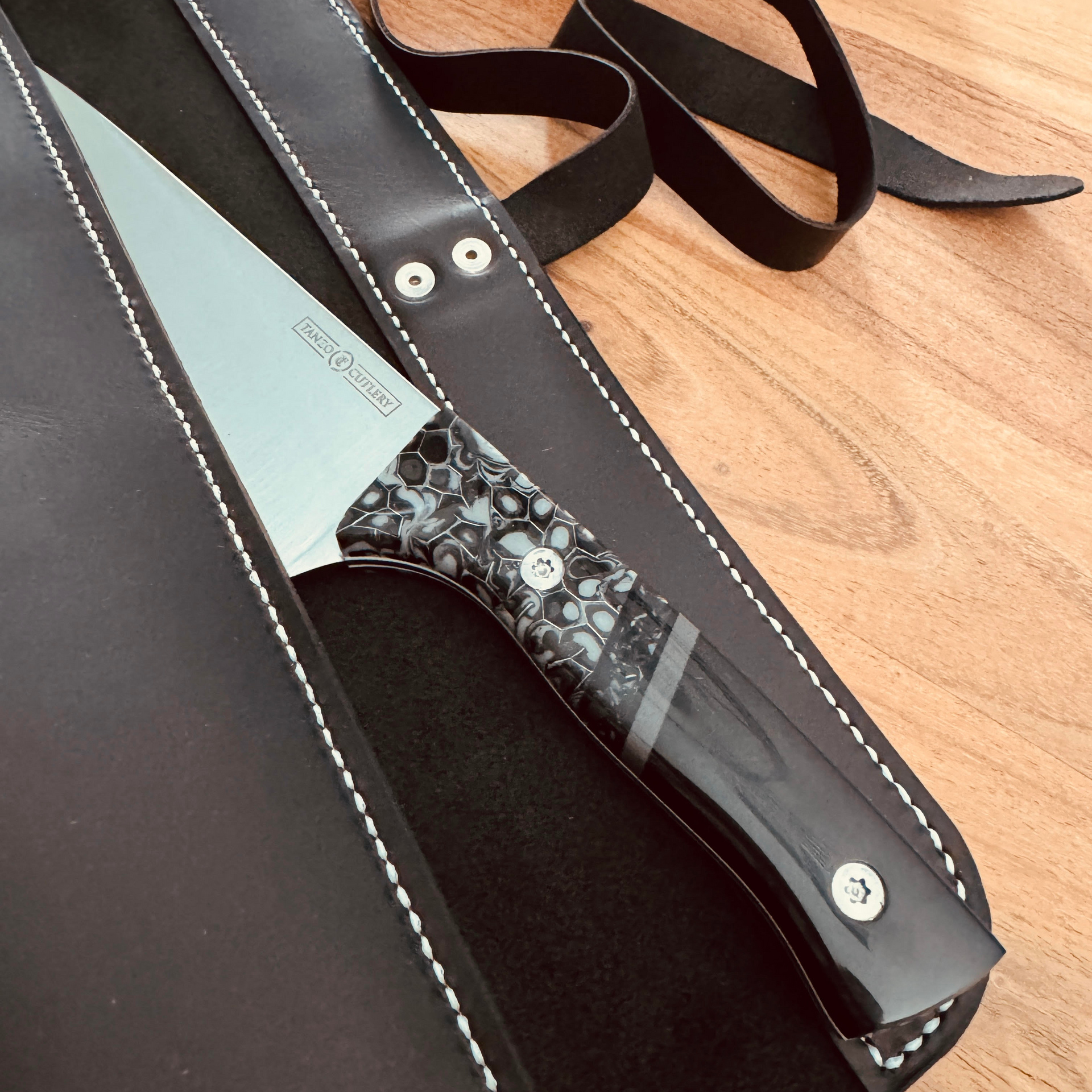 TANZO CUTLERY professional chef knife with a patterned resin handle and a handcrafted black leather sheath.