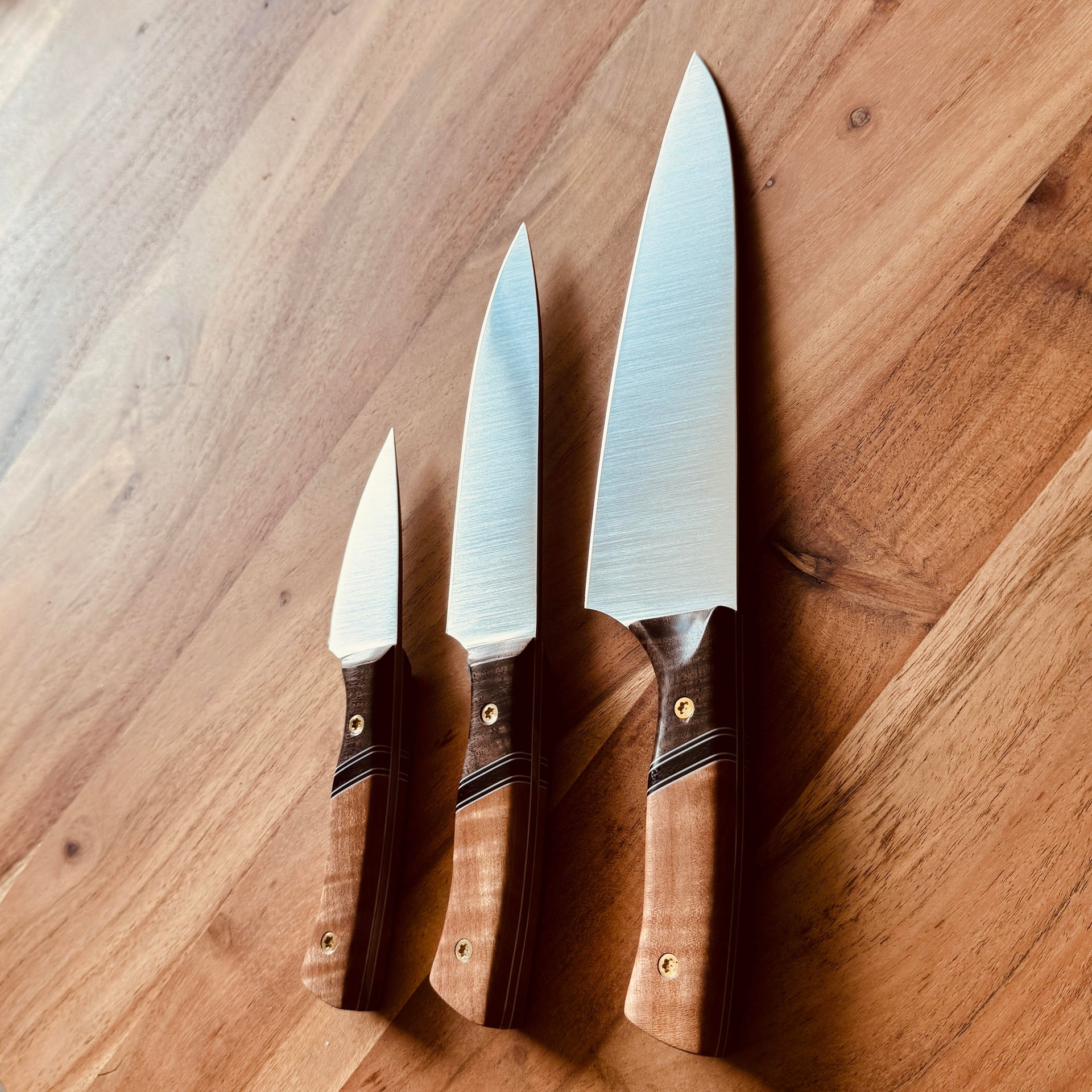 TANZO CUTLERY set of three handcrafted chef knives with polished steel blades and ergonomic two-tone wood handles.