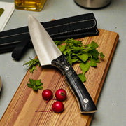 TANZO CUTLERY professional chef knife with patterned handle and leather sheath on a wooden cutting board with herbs