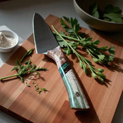 TANZO CUTLERY professional chef knife with a unique patterned handle on a wooden cutting board with fresh herbs