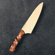 TANZO CUTLERY professional chef knife with a sharp steel blade and an ornate, patterned handle on a dark background.