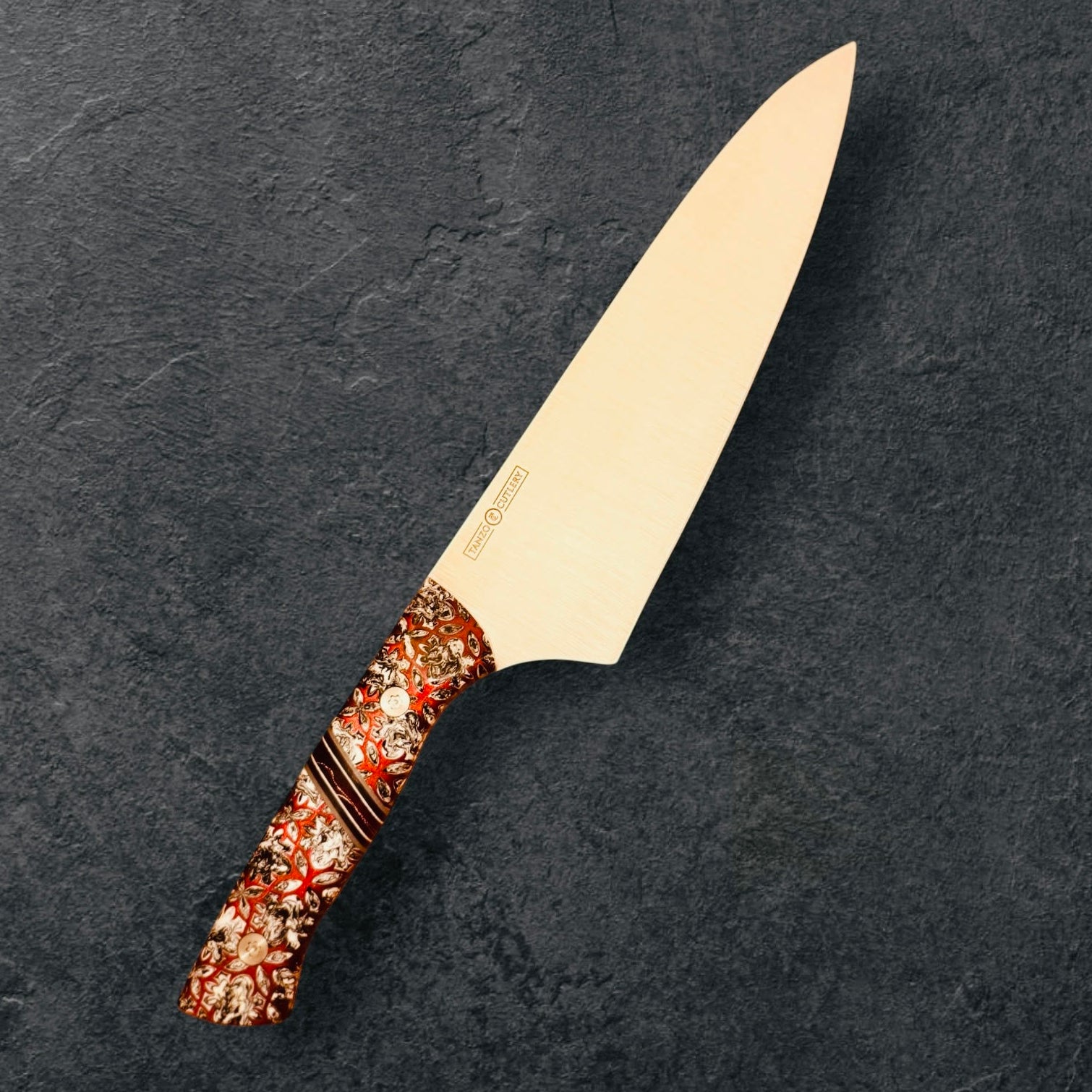 TANZO CUTLERY professional chef knife with a sharp steel blade and an ornate, patterned handle on a dark background.